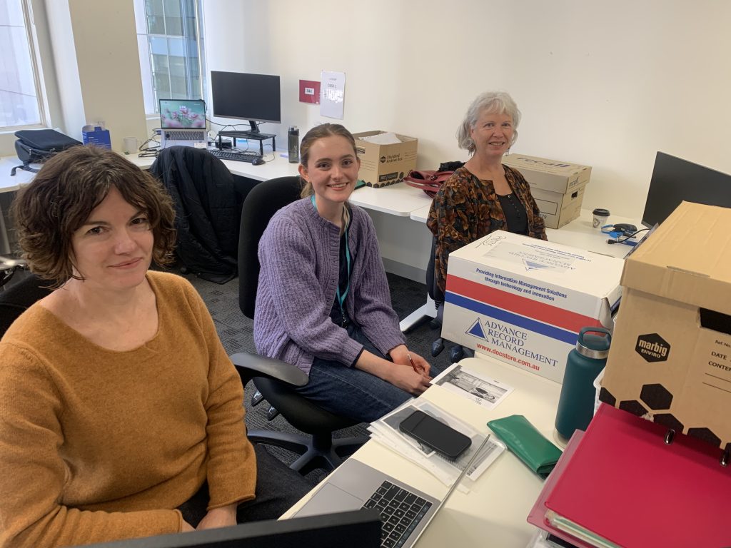 Three female historians sitting by a desk with boxes of archived material